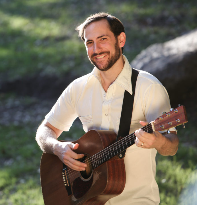 Ben Kramarz smiling with his guitar outdoors