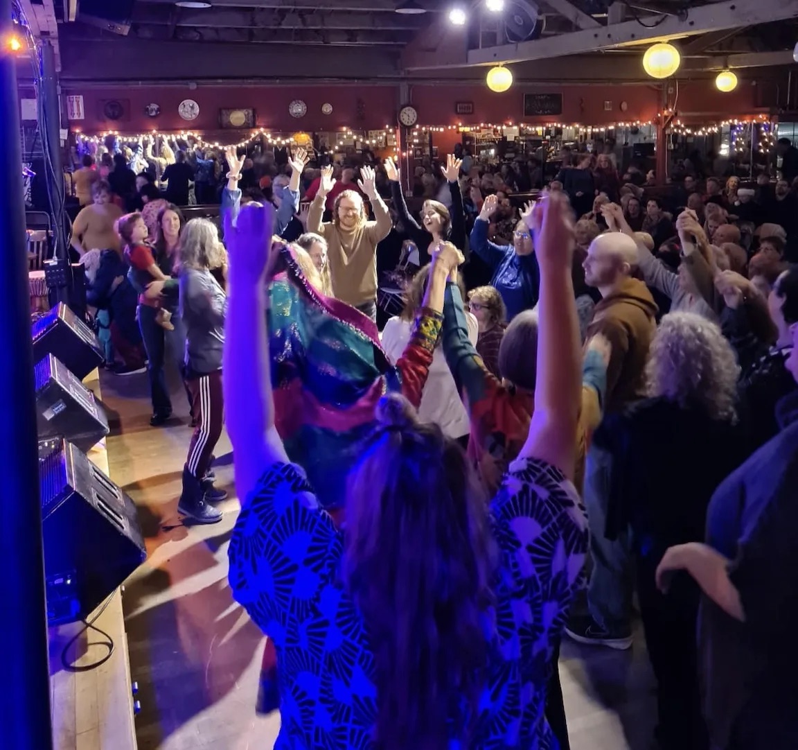 A crowd with hands raised at the Interfaith Holiday Concert