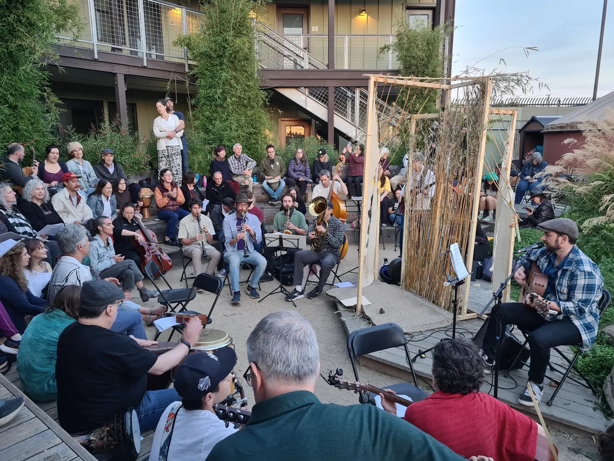 Ben with his guitar leading a circle of musicians and singers at an outdoor community jam